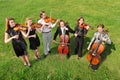 Six violinists stand semicircle on grass and play Royalty Free Stock Photo