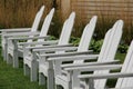 Six white Adirondack chairs on manicured lawn