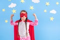 Six year blonde girl dressed like superhero having fun at home. Kid on the background of bright blue wall. Royalty Free Stock Photo