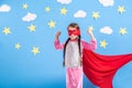 Six year blonde girl dressed like superhero having fun at home. Kid on the background of bright blue wall. Royalty Free Stock Photo