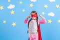 Six year blonde girl dressed like superhero having fun at home. Kid on the background of bright blue wall. Royalty Free Stock Photo