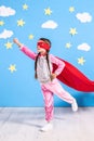 Six year blonde girl dressed like superhero having fun at home. Kid on the background of bright blue wall. Royalty Free Stock Photo