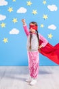 Six year blonde girl dressed like superhero having fun at home. Kid on the background of bright blue wall. Royalty Free Stock Photo