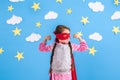 Six year blonde girl dressed like superhero having fun at home. Kid on the background of bright blue wall. Royalty Free Stock Photo