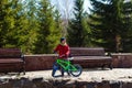 Six-year-old boy in a warm jacket and hat holds a two-wheeled bike outdoors, wooden benches Royalty Free Stock Photo