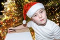 Six year old cute little boy with red christmas cap writing letter to Santa Claus near the Christmas tree indoors. Bright New Year Royalty Free Stock Photo