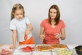 Six year old girl takes plate of cutting tomatoes for pizza under the supervision of mum