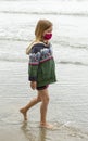 Young girl wearing a jacket and pink face mask at the beach Royalty Free Stock Photo