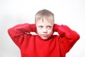 Six-years old boy in red hoodie closing ears with his hands on grey background. Autism concept