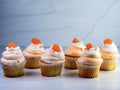 Six, 6, yellow cupcakes lined up with orange and white creamsicle frosting swirled up high and an orange gum drop candy on top. Royalty Free Stock Photo