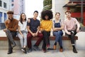 Six young adult friends sitting in a row on a bench in a city street smiling to camera, full length Royalty Free Stock Photo