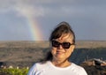 Sixty-three year-old female Korean tourist standing with a rainbow in the background in Hawaii Volcanoes National Park.