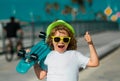 Skateboarder child boy in skate park. Kid boy with skateboard. Excited child with thumb up, street portrait close up