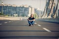 Skateboarder sitting on his skateboard at highway bridge