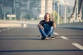 Skateboarder sitting on his skateboard at highway bridge