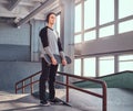 Young skateboarder standing next to a grind rail in skatepark indoors, holding his board and looking away. Royalty Free Stock Photo