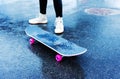 Skateboarding Skateboard with pink wheels and legs of a novice skateboarder in white sneakers on wet asphalt after rain. The first