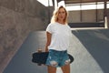 Skater Girl With Skateboard Portrait. Teenager In Casual Outfit Posing Against Concrete Ramp At Skatepark.