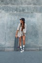 Skater Girl At Skatepark. Full-Length Portrait Of Female Hipster In Casual Outfit With Skateboard Against Concrete Wall. Royalty Free Stock Photo