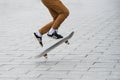 Skater legs wearing black sneakers by Adidas jumping with skate board in the street