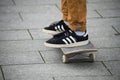 Skater legs wearing black sneakers by Adidas standing on skate board in the street