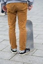 Skater legs wearing black sneakers by Adidas standing with skate board in the street