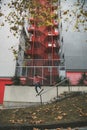 Skater with pink sweatshirt on a snakeboard grind a railing of an urban street with a red and gray building in the background