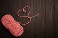 a skein of pink yarn and a heart of thread on a dark wooden background