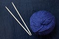 Skein of purple yarn with bamboo knitting needles with black slate background