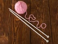 Skein of soft pink yarn and knitting needles on wooden surface