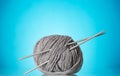 Skein of thick, grey yarn and knitting needles on blue