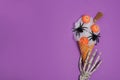 Skeleton hand holding Halloween icecream made with spider web, witch\'s broom and candies pumpkins on purple background Royalty Free Stock Photo