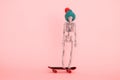 skeleton wearing knitted hat riding skateboard against pastel pink background