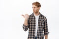 Skeptical redhead man cringe from something bad, looking and pointing left with judging disappointed look, having doubts Royalty Free Stock Photo