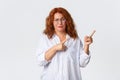 Skeptical and unamused redhead middle-aged woman smirk displeased, having doubts, pointing fingers upper right corner Royalty Free Stock Photo