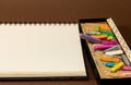 Sketch notebook, blank page and a box of used chalk colors sticks on brown background.