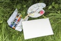 Sketchbook, watercolor paints and the artist`s palette lie in the grass, top view