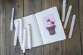 Sketching chocolate cupcake in notebook. All placed on wooden table notebook and markers. Hobby. Drawing cupcake. Top