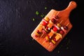 Skewered party appetizers with meat, cheeses and pickles on a serving board, top view on a dark background