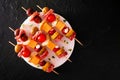 Skewered party appetizers with meat, cheeses and pickles on a serving plate, top view over dark stone