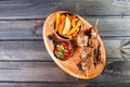 Skewers of Meat with sauce and potatoes fries in a bucket on wooden cutting board. Royalty Free Stock Photo
