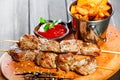 Skewers of Meat with sauce and potatoes fries in a bucket on wooden cutting board Royalty Free Stock Photo