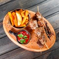 Skewers of Meat with sauce and potatoes fries in a bucket on wooden cutting board Royalty Free Stock Photo