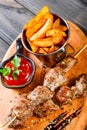Skewers of Meat with sauce and potatoes fries in a bucket on wooden cutting board. Royalty Free Stock Photo