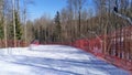 At the ski center, the slopes are fenced with a mesh fence with metal poles, behind which there are trees. The sun shines brightly
