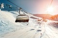 Ski lift empty ropeway on hilghland alpine mountain winter resort on bright sunny evening . Ski chairlift cable way with people Royalty Free Stock Photo