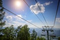Ski lift in the mountains on sunny day against blue sky, white clouds, green hills and mountain lake. Mountain valley with cable Royalty Free Stock Photo