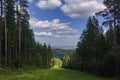 Ski slope in the summer against a background of coniferous forest and blue sky with white clouds Royalty Free Stock Photo