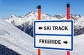 Ski track and freeride delimitation sign with arrows showing opposite directions against snowy mountain blue sky winter