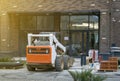 Skid loader stands in front of entrance to new multi-storey house and waits for garbage to be loaded into  bucket. Mini bulldozer Royalty Free Stock Photo